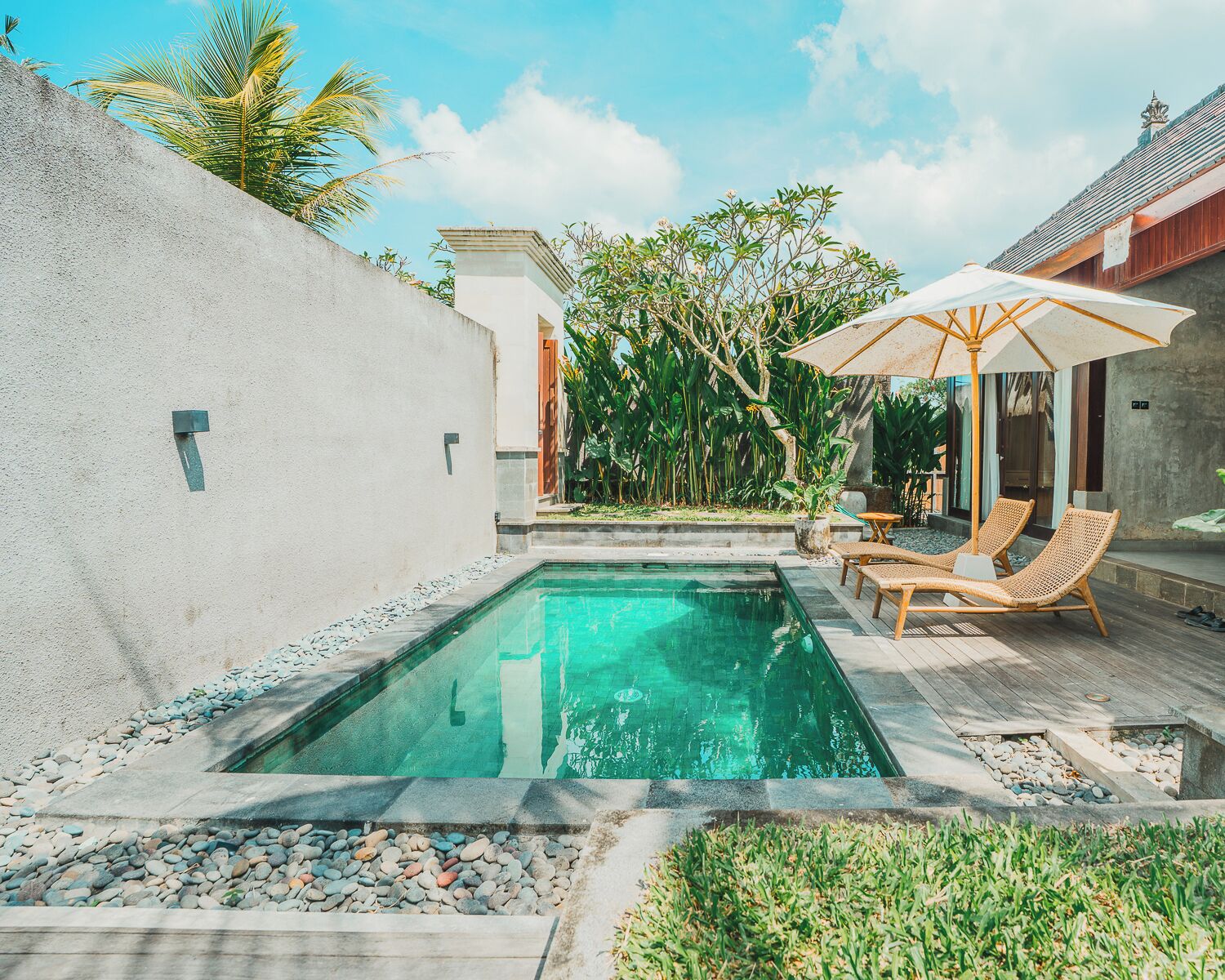 A swimming pool with a wooden deck, lounge chairs, and a covered seating area.