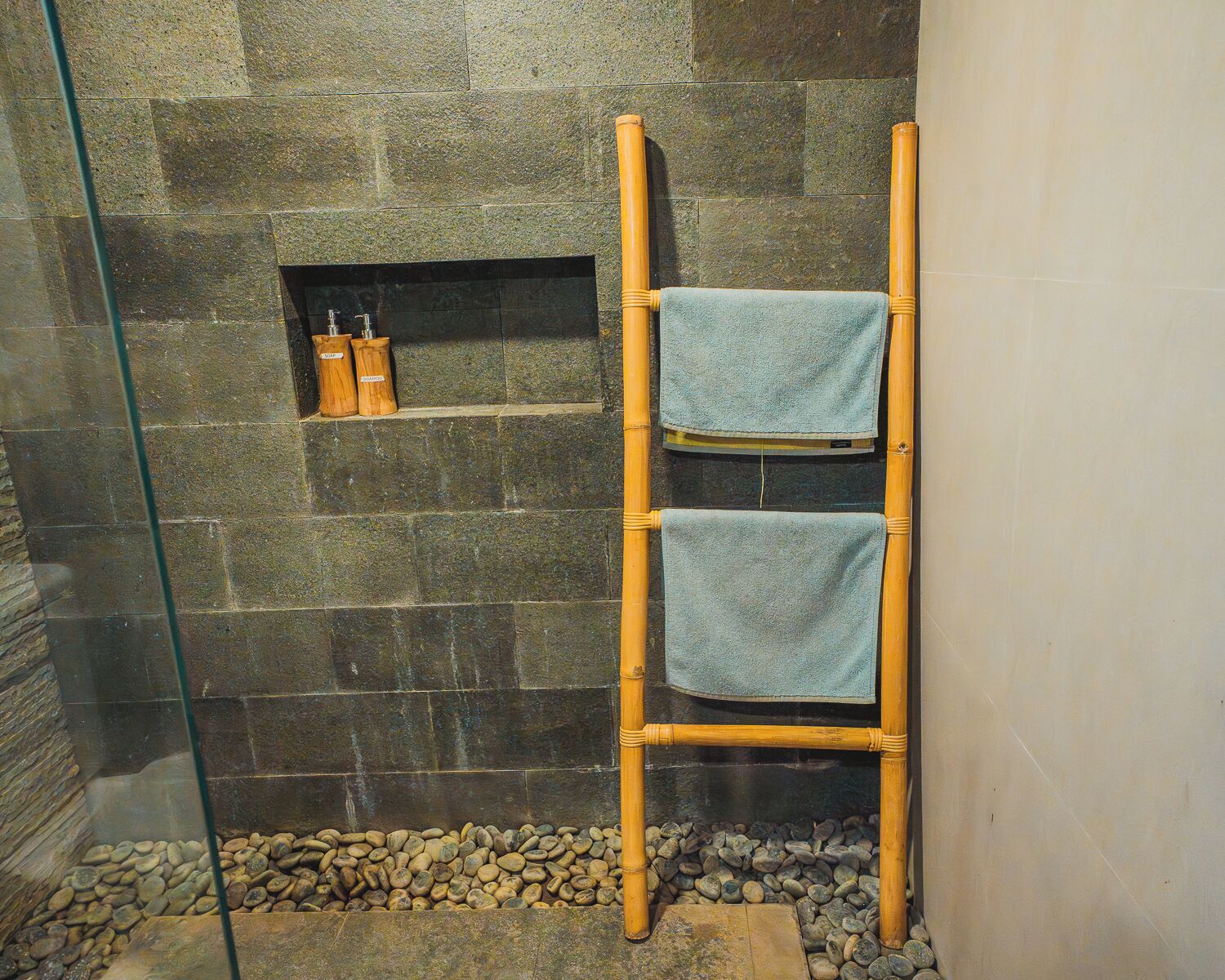 A bathroom with a stone wall, a bamboo towel rack, and a small shelf with bottles.