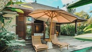 A poolside area with two wicker lounge chairs, a wooden umbrella, and a view of a building with a tiled roof. - Jero Kelodan Villa (Tabanan)