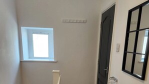 Un couloir étroit avec un plancher en bois, une petite fenêtre, une porte et un interrupteur fixé au mur.