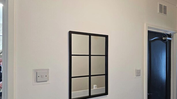 Un couloir avec une fenêtre fixée au mur, une porte et un interrupteur.