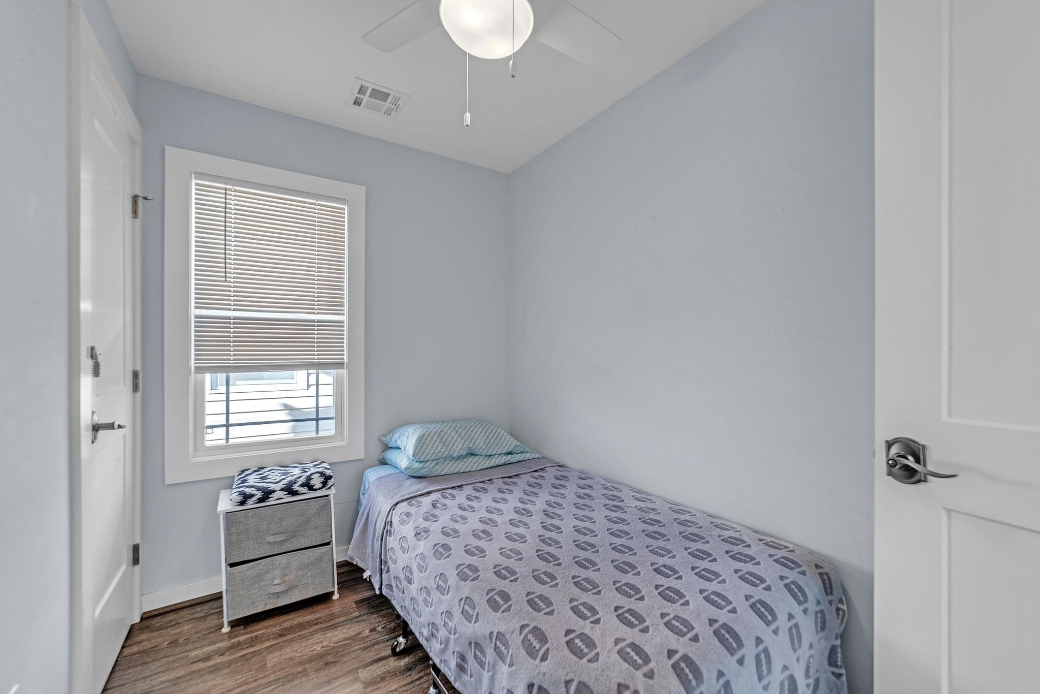 A small, neatly arranged bedroom with a single bed, a bedside table, and a window with blinds.