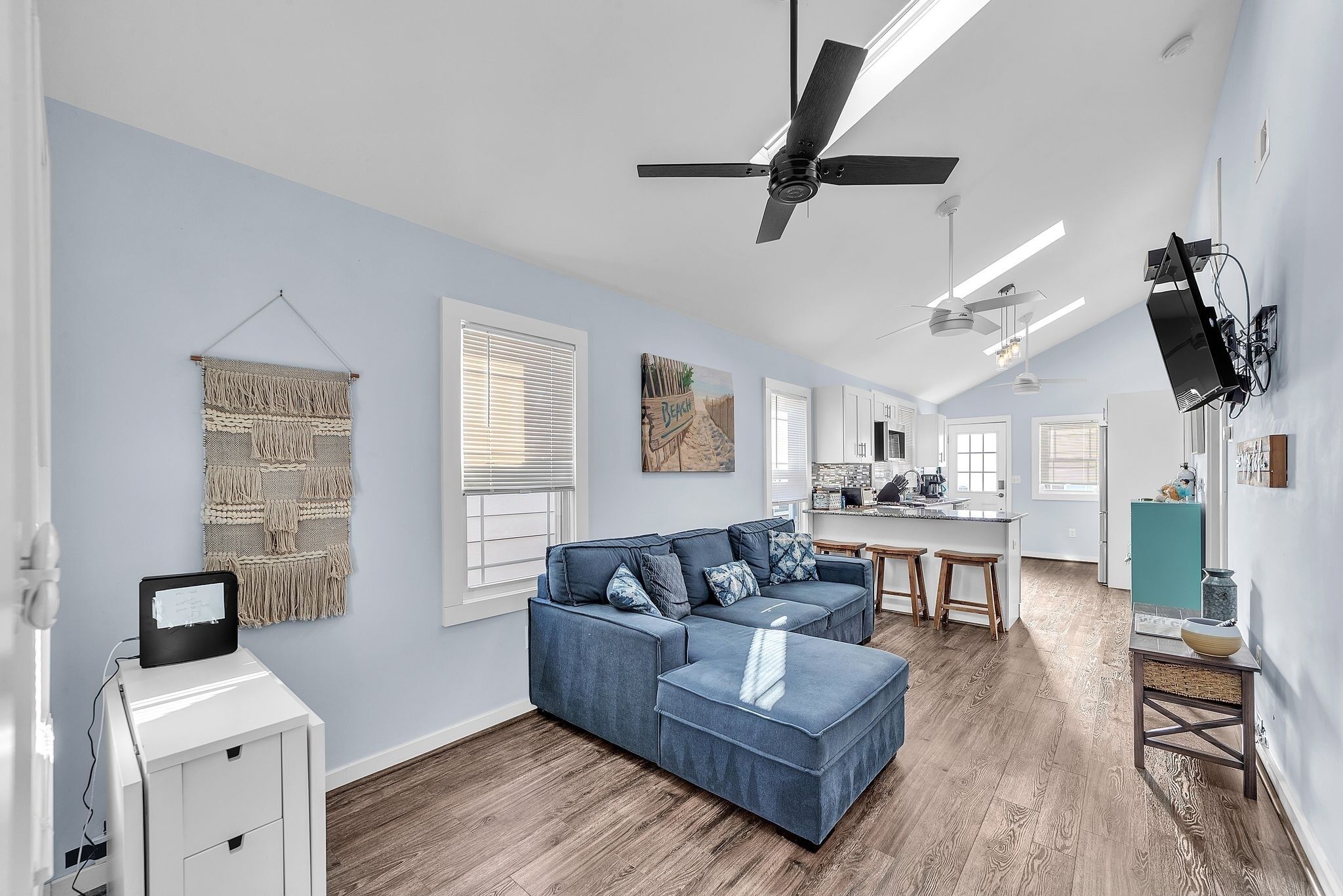 Un salon moderne avec un canapé d’angle, un petit coin cuisine et un ventilateur de plafond.