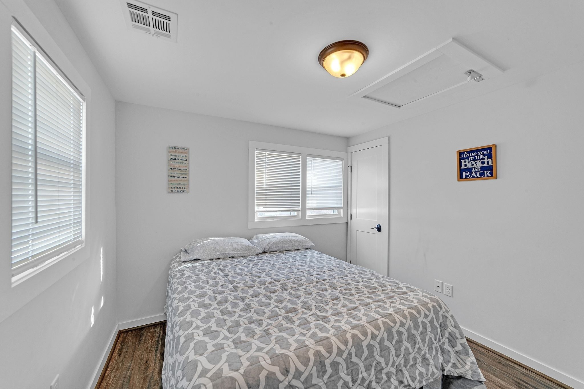 A bedroom with a bed, two windows with blinds, a door, and a ceiling light fixture.