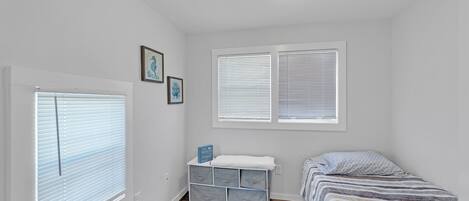 Un dormitorio con una cama, una mesita de noche, un tocador y una ventana con persianas.