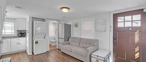 A compact living space with a kitchenette, a sofa, a small table, and a door with a window.