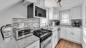 Una cucina moderna con mobili bianchi, piano cottura a gas, forno a microonde integrato e forno in acciaio inossidabile.