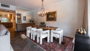 Un coin repas avec une table en bois, des chaises blanches et un lustre.