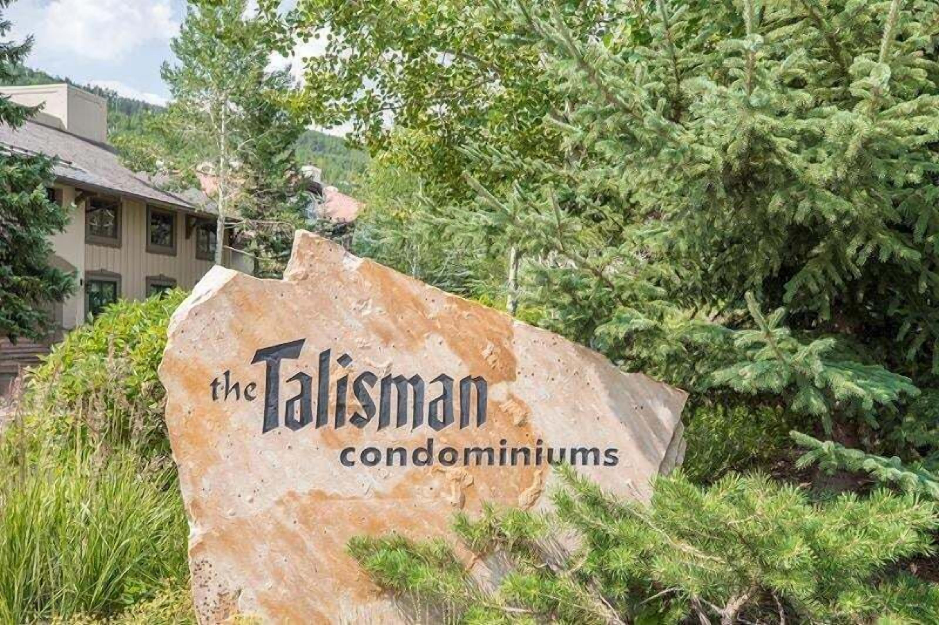 Une enseigne indiquant « Les condominiums Talisman », avec un décor naturel en arrière-plan.