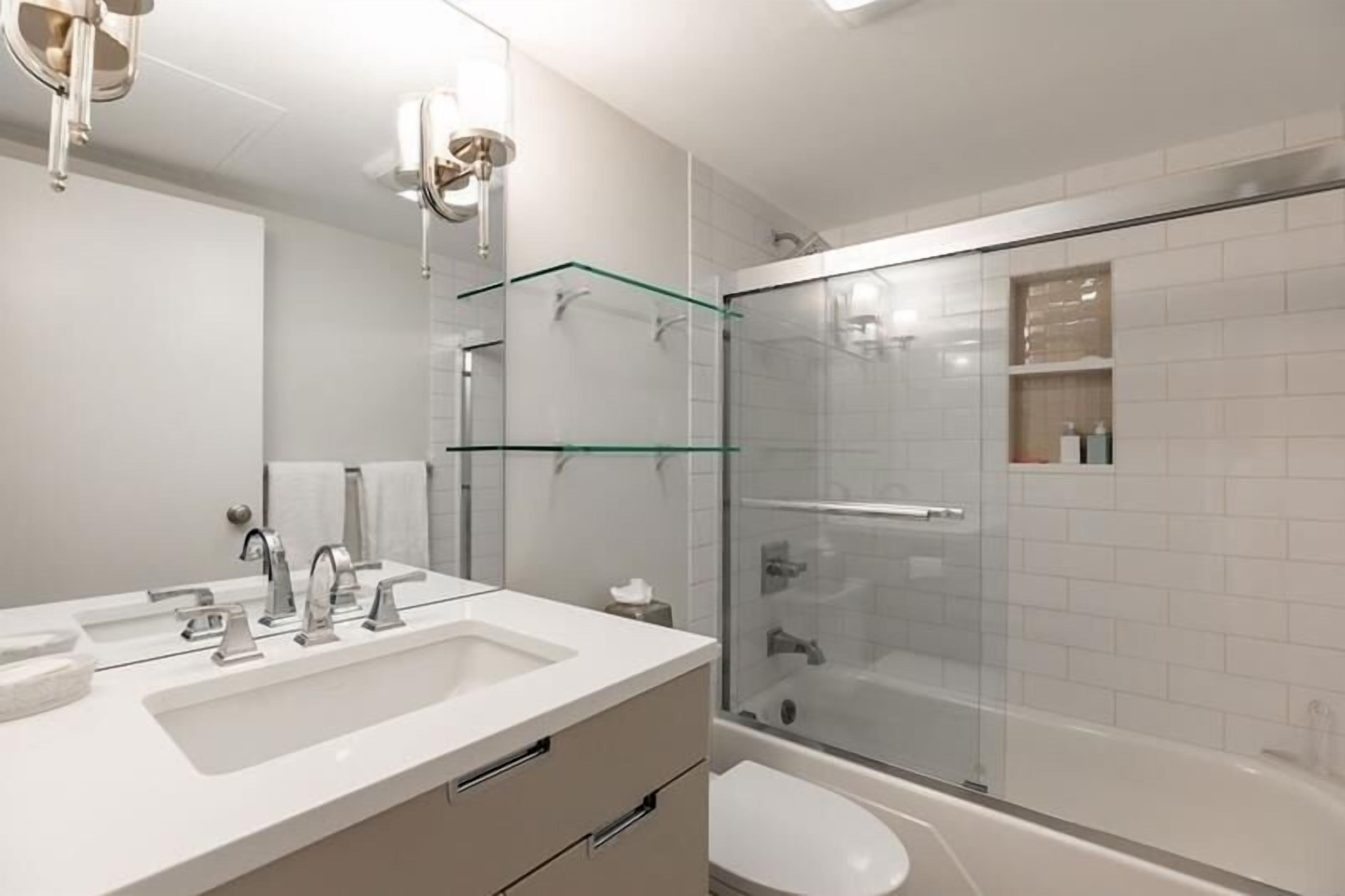 A modern bathroom with a glass-enclosed shower, a white sink with two basins, and a large mirror.