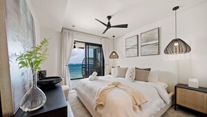 Un dormitorio moderno con una cama grande, ventilador de techo y vista al océano.