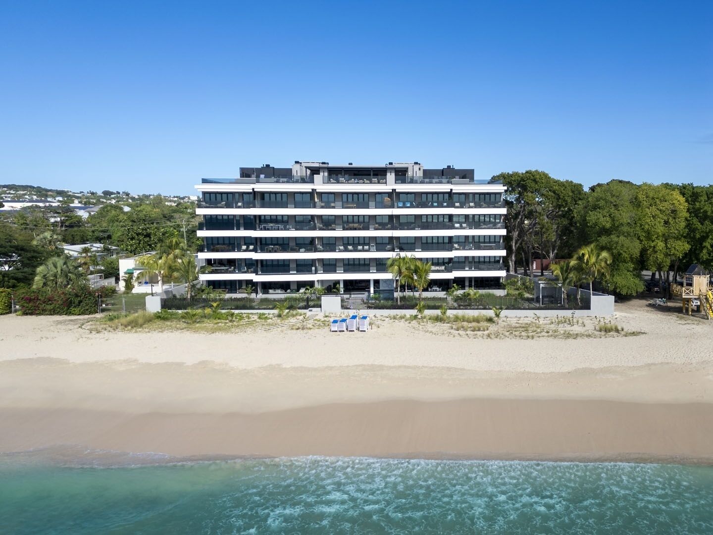 Um hotel de vários andares com varandas, situado numa praia com vista para o oceano.