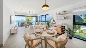 A modern living room with a dining area, large windows, and a view of the ocean. - Allure 205 3 Bedroom Apts (Bridgetown)