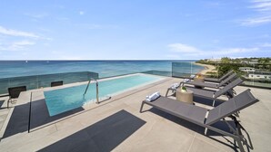 A rooftop infinity pool with lounge chairs, a glass balustrade, and a view of the ocean.