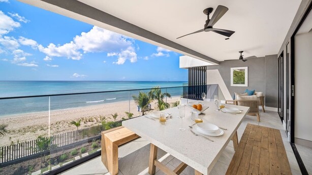 A balcony with a dining table set for two, overlooking a beach.