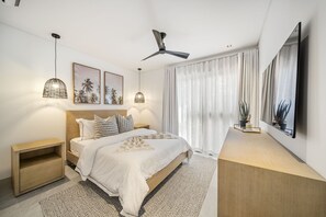 Et moderne soveværelse med seng, sengeborde, loftventilator, kunst og et stort vindue med gardiner.