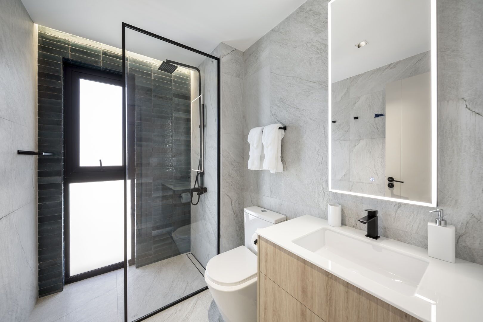 A modern bathroom with a glass-enclosed shower, a white toilet, a wooden vanity, and a large mirror.