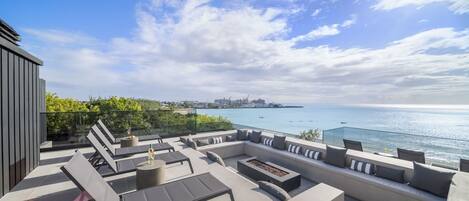 A rooftop terrace with a view of the sea, modern outdoor furniture, and a glass balustrade.