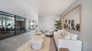 Un vaste espace de vie au design moderne, comprenant un ensemble de canapés blancs, une table basse ronde et un grand tableau mural.