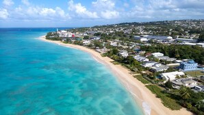 An aerial view of a coastal town with a beach, buildings, and clear blue waters. - Allure 505 3 Bedroom Apts (Bridgetown)