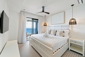 A modern hotel room with a large bed, a ceiling fan, a TV, a bedside table, and a view of the ocean. - Allure 403 3 Bedroom Apts (Bridgetown)