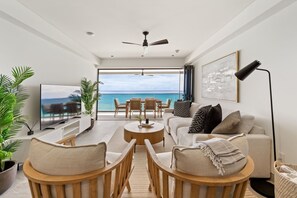 A modern living room with a TV, sofa, chairs, a coffee table, and a view of the ocean. - Allure 403 3 Bedroom Apts (Bridgetown)