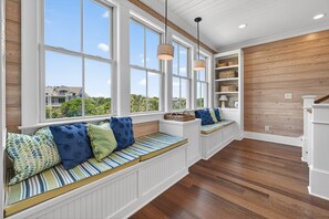 A room with large windows, built-in seating, wooden floors, and a white wall with shelves.
