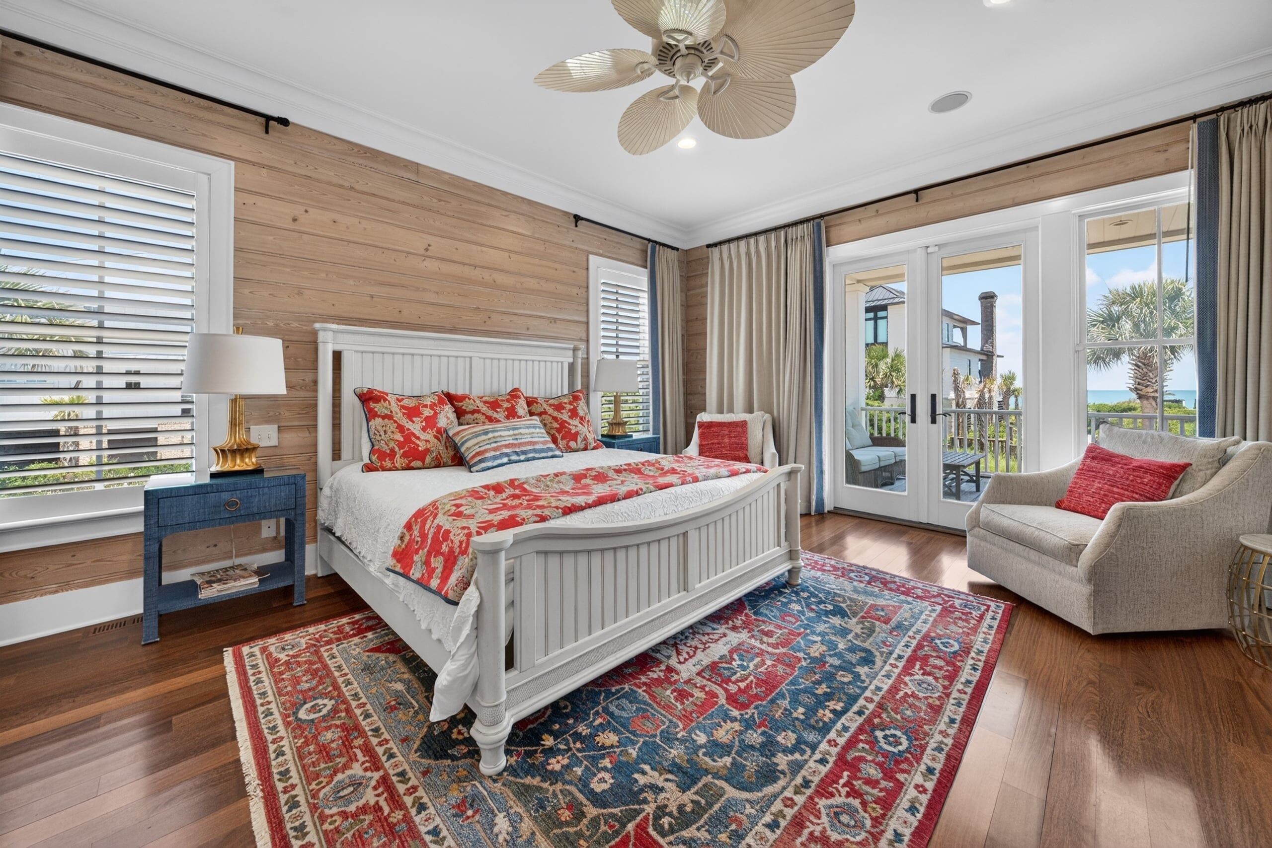 A bedroom with a large bed, a chair, a ceiling fan, and a view of the outdoors.