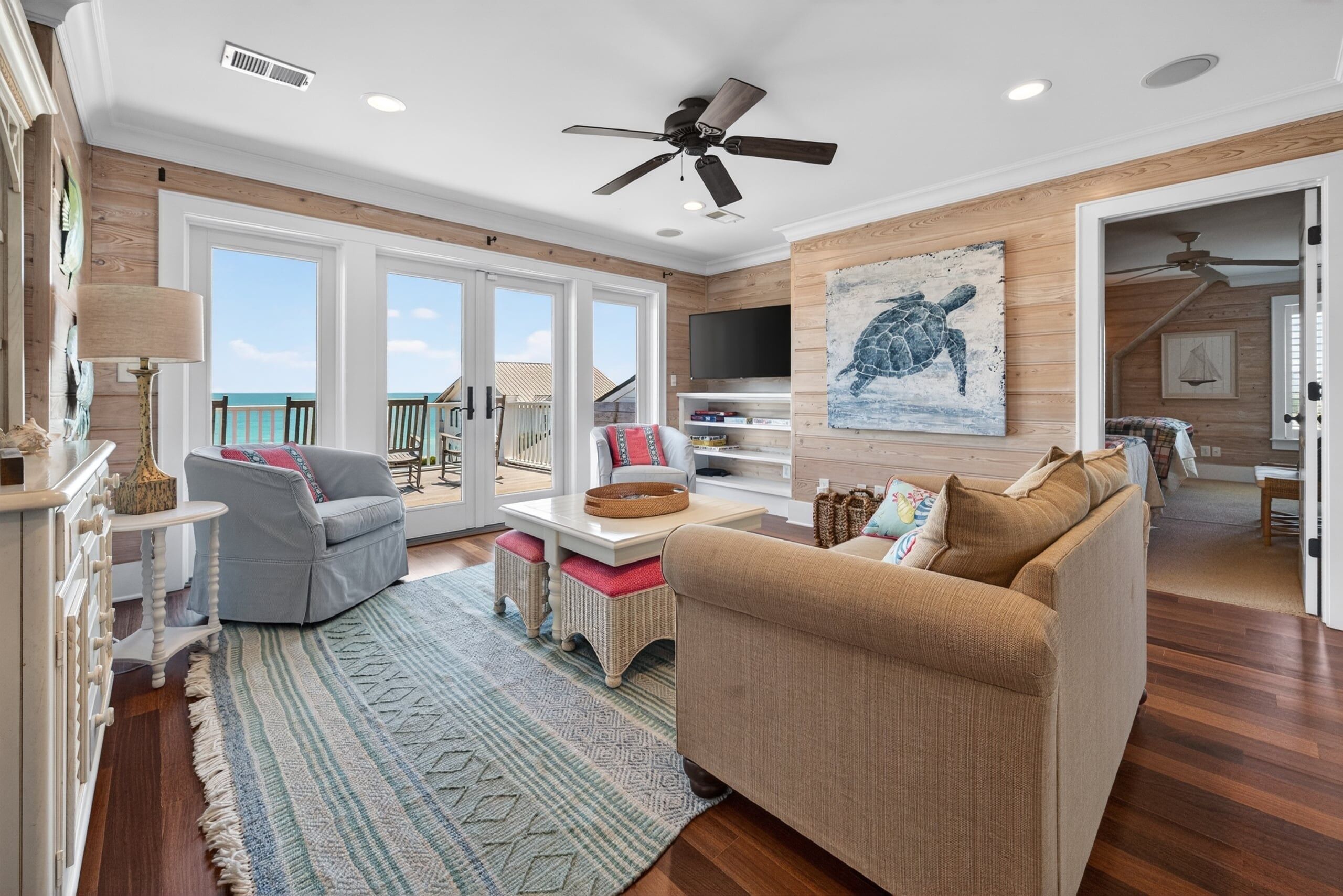 A spacious living room with a large window, a ceiling fan, and a television.