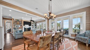 A spacious living area with a wooden dining table, woven chairs, and a large window offering a view of the ocean. - Sun And Solitude 7 Bedroom Home (Georgetown)