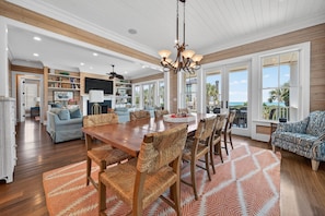 A spacious living area with a wooden dining table, woven chairs, and a large window offering a view of the ocean.