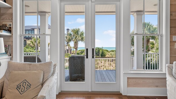 A room with a sliding glass door leading to a balcony with a view of the ocean and palm trees. - Sun And Solitude 7 Bedroom Home (Georgetown)