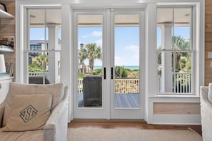 Ein Zimmer mit einer Schiebeglastür, die auf einen Balkon mit Blick auf das Meer und Palmen führt.
