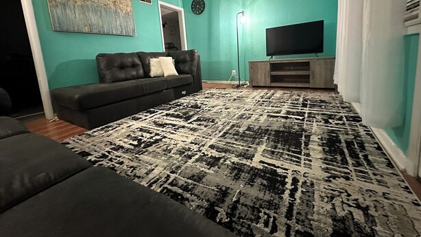 A living room with teal walls, a black sofa, a patterned rug, a flat-screen TV on a wooden stand, and a painting on the wall. - Charming 2-bedroom house in Aberdeen with WiFi and AC (Aberdeen)
