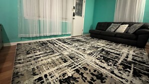 A living room with a black sofa, patterned rug, and teal walls. - Charming 2-bedroom house in Aberdeen with WiFi and AC (Aberdeen)