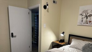 A bedroom with a bed, a bedside table with a lamp, a door, and a wall-mounted light fixture. - Charming 2-bedroom house in Aberdeen with WiFi and AC (Aberdeen)