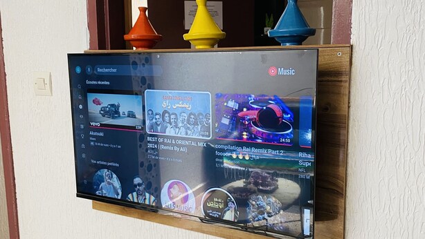 A flat-screen TV mounted on a wall displaying a music streaming service interface with various music tracks and artists visible. - Apartment in the center of Tiznit (tiznit neuf)