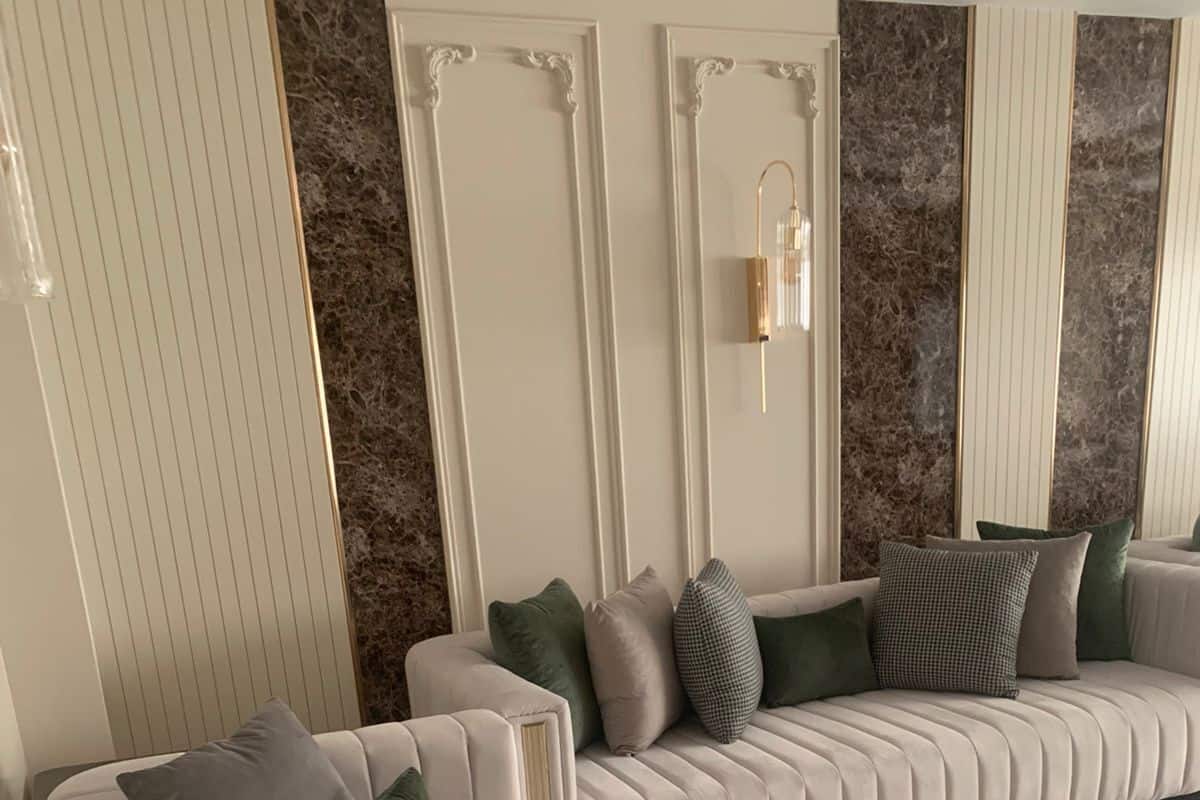 A modern living room with a beige sofa and a matching armchair, both with multiple cushions.