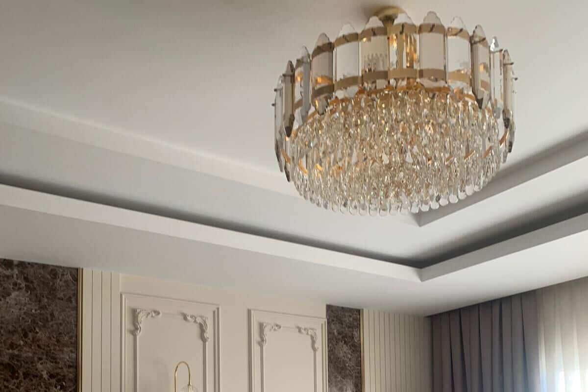 A modern living room with a plush sofa, a round armchair, a chandelier, and a wall-mounted air conditioner.