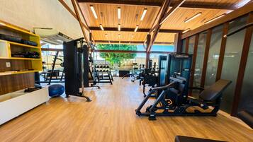Academia com piso de madeira, equipamentos de exercício e vista para o exterior.