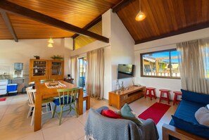 A spacious living area with a dining table, chairs, a sofa, a TV, and a large window.