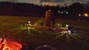 Une scène nocturne en plein air avec un feu de camp, un tronc d’arbre et une zone herbeuse.