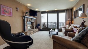 A living room with a stone fireplace, a large window, and a balcony. - BT201 | Amazing Views | Ski In | Ski Lockers | Indoor Pool (Steamboat Springs)