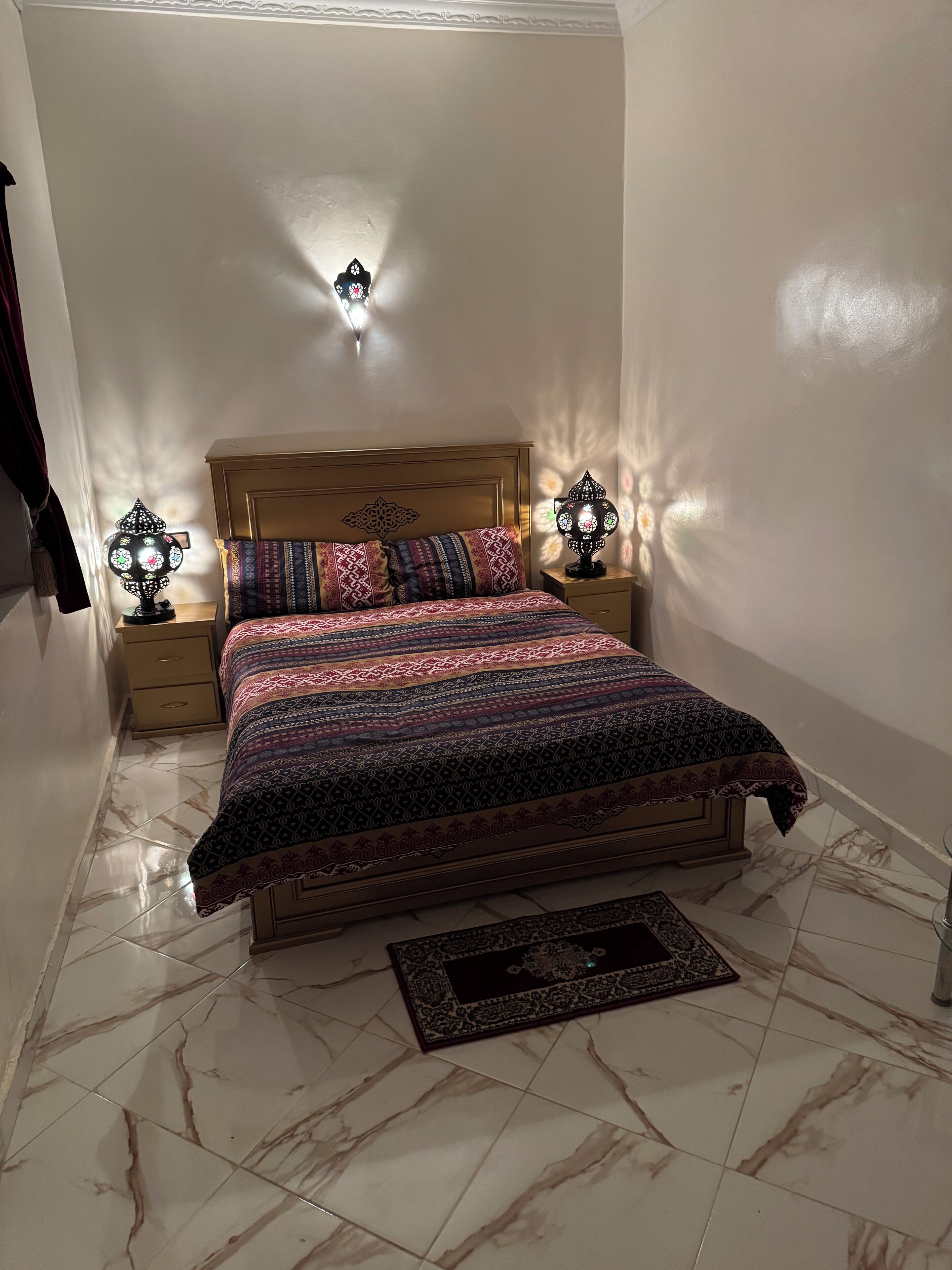 Una camera da letto con un letto di legno, biancheria da letto decorata, due lampade a parete e un pavimento in marmo.
