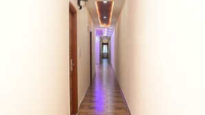 A long, narrow hallway with wooden flooring and white walls. - Hotel Zeke Avenue (Bengaluru)