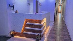 A reception area with a marble counter, wooden steps, and a hallway with wooden flooring. - Hotel Zeke Avenue (Bengaluru)