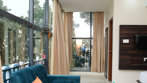 A modern hotel room with a large window, a teal sofa, a round coffee table, and a TV mounted on the wall. - Hotel Zeke Avenue (Bengaluru)