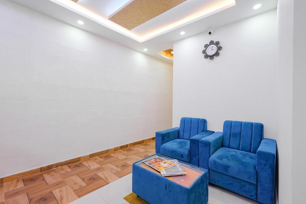 A modern room with a wooden herringbone floor, two blue upholstered chairs, a glass coffee table with magazines, and a decorative clock on the wall.