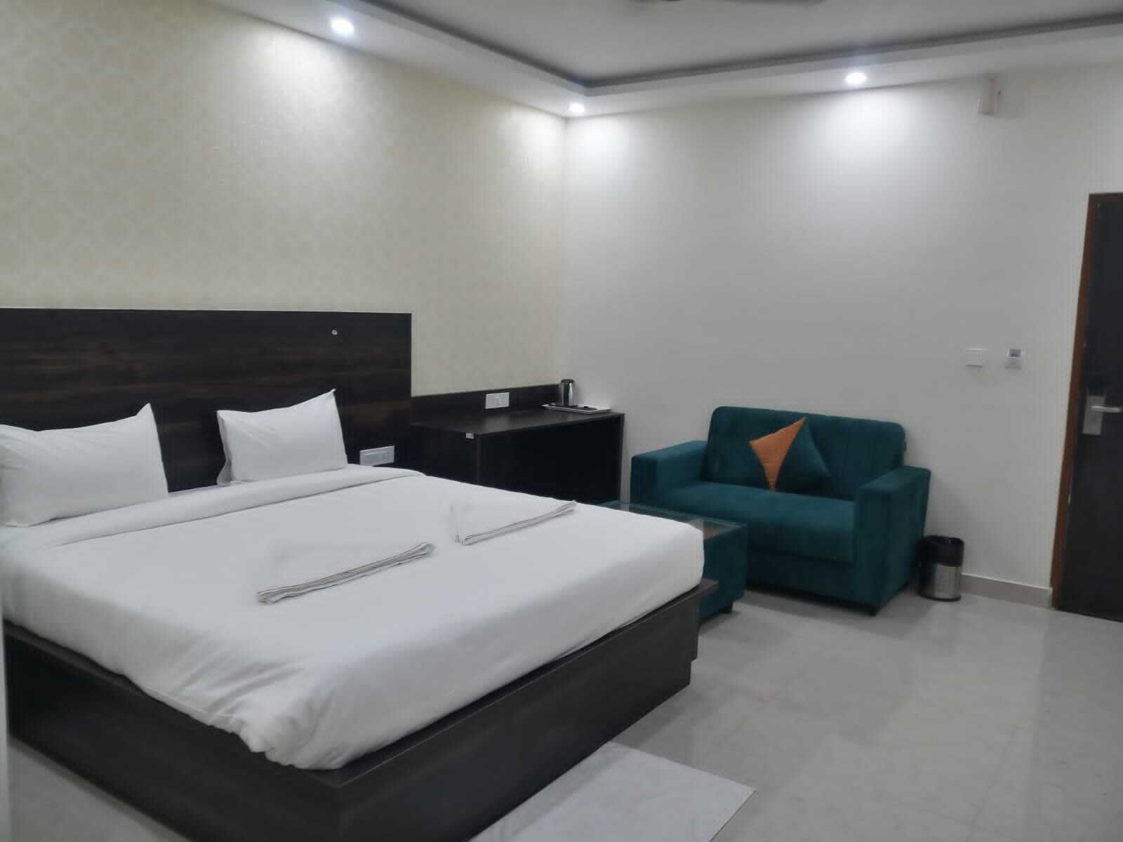 Una habitación de hotel moderna con una cama grande, un escritorio pequeño, un sofá color turquesa y un cubo de basura.