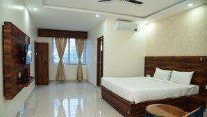 A modern bedroom with a wooden bed, a TV mounted on the wall, a ceiling fan, and a window with curtains. - Hotel Zeke Avenue (Bengaluru)